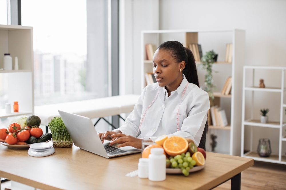 Serious,Multicultural,Lady,In,Doctor's,Coat,Typing,On,Modern,Laptop